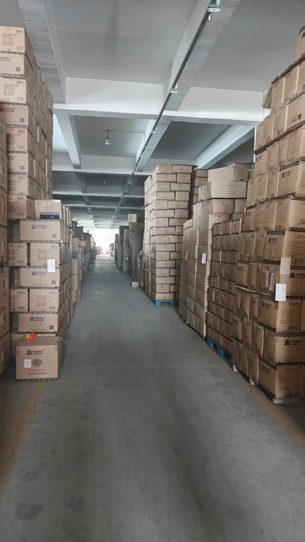 Packed glassware cartons stored along a central warehouse aisle.