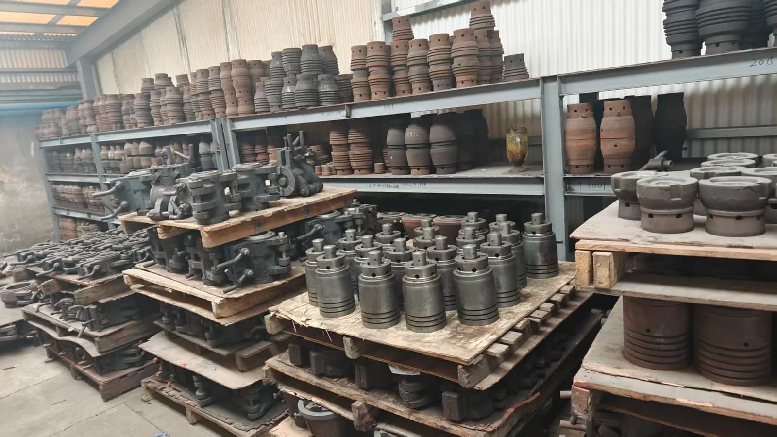 Metal molds and tooling in a range of shapes, arranged on shelves and pallets.